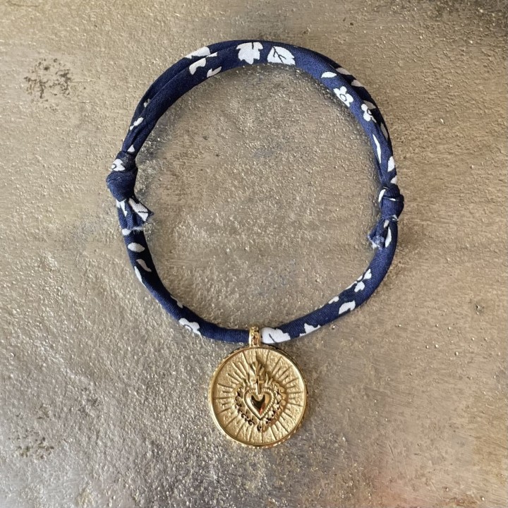 bracelet en coton Liberty coulissant mettant en valeur une médaille ex voto du Cœur Sacré en acier doré inoxydable.