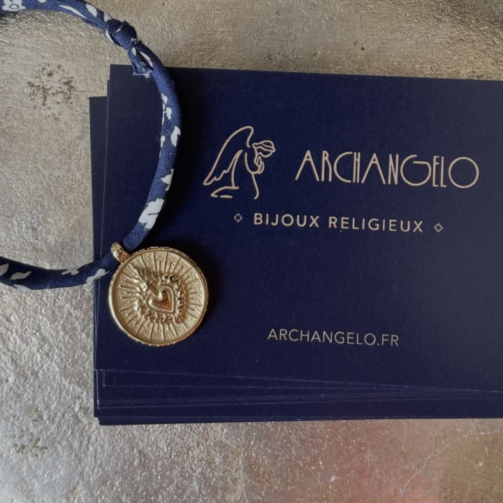 bracelet en coton Liberty coulissant mettant en valeur une médaille ex voto du Cœur Sacré en acier doré inoxydable.