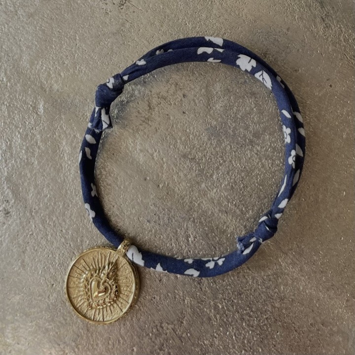 bracelet en coton Liberty coulissant mettant en valeur une médaille ex voto du Cœur Sacré en acier doré inoxydable.